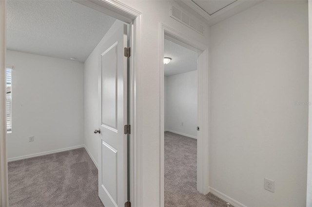 corridor with a textured ceiling and light carpet