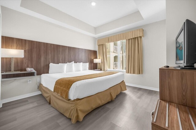 bedroom featuring baseboards, wood finished floors, and a tray ceiling