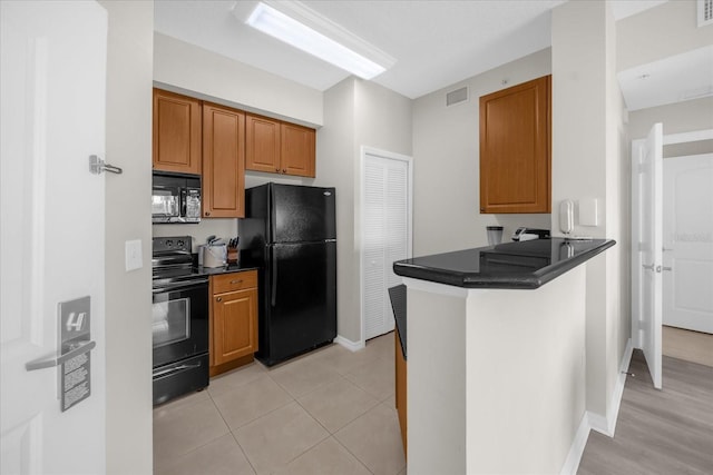 kitchen with brown cabinets, dark countertops, a peninsula, visible vents, and black appliances