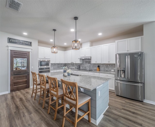 kitchen featuring a breakfast bar area, appliances with stainless steel finishes, a kitchen island with sink, light stone countertops, and white cabinets