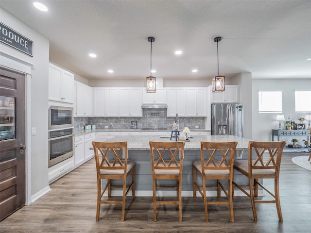 kitchen with stainless steel appliances, an island with sink, white cabinets, and a kitchen bar