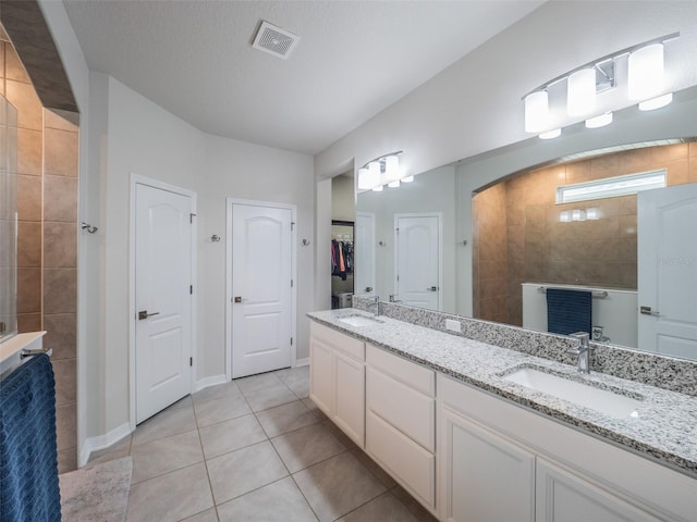 bathroom featuring tile patterned floors, a tile shower, vanity, and a textured ceiling