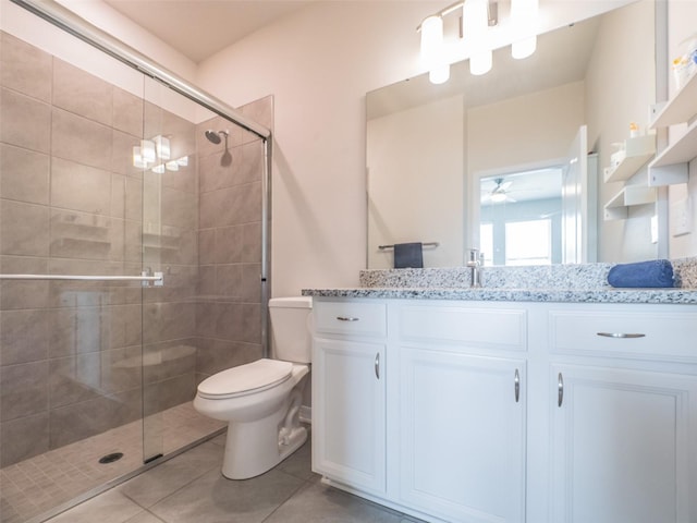 bathroom featuring tile patterned floors, toilet, vanity, a shower with door, and ceiling fan