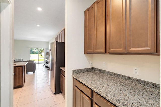 kitchen featuring light tile patterned flooring, stainless steel refrigerator, and light stone counters