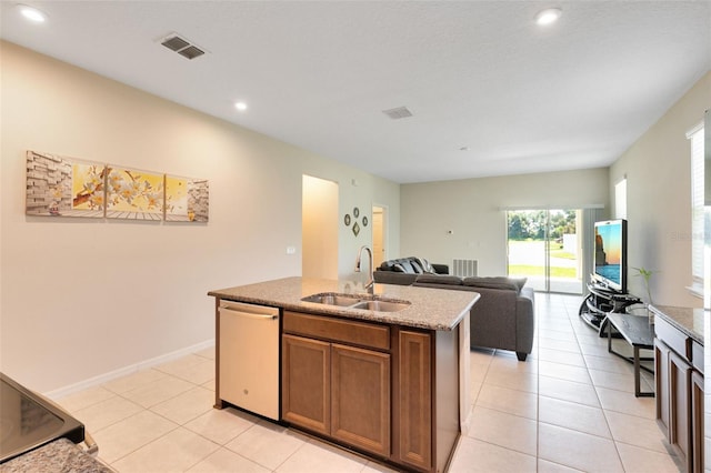 kitchen with a kitchen island with sink, light stone countertops, sink, stainless steel dishwasher, and light tile patterned flooring