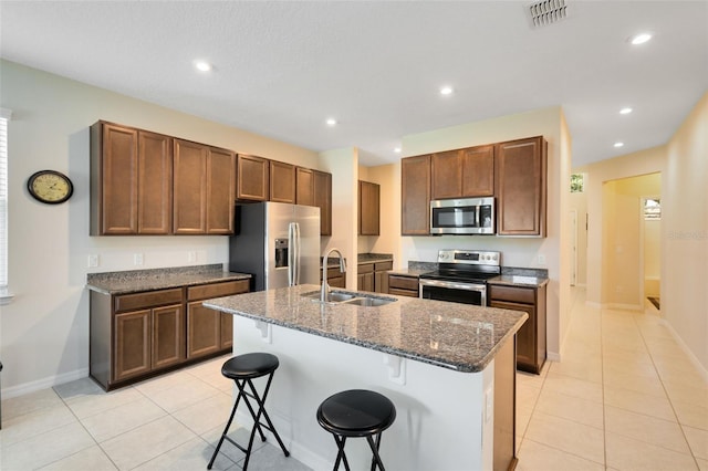 kitchen featuring stainless steel appliances, an island with sink, dark stone counters, a kitchen bar, and sink