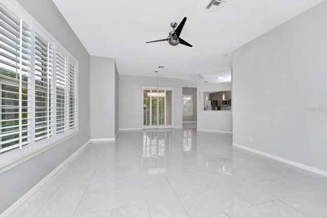 unfurnished living room featuring ceiling fan with notable chandelier and plenty of natural light