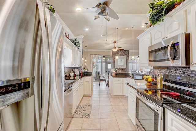 kitchen featuring white cabinets, crown molding, light tile patterned floors, decorative light fixtures, and stainless steel appliances