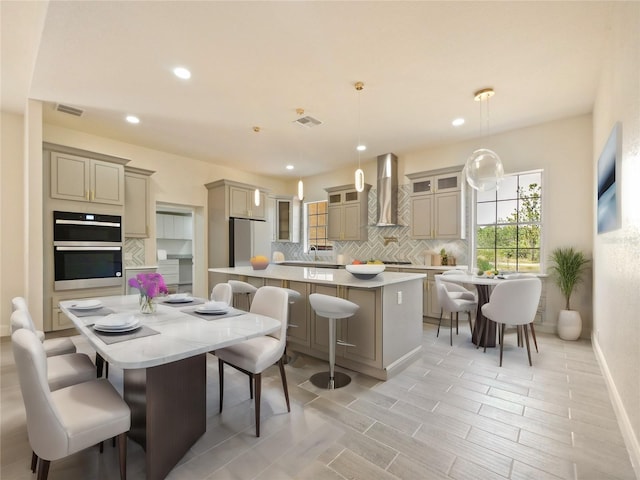 kitchen with backsplash, a breakfast bar, wall chimney range hood, decorative light fixtures, and a center island