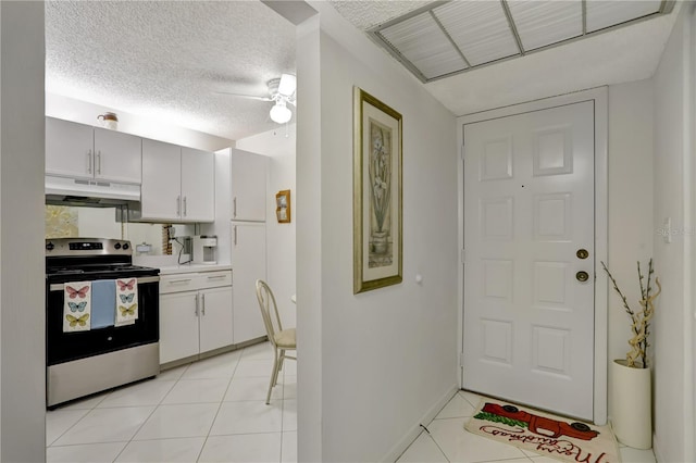 kitchen featuring white cabinets, light tile patterned floors, a textured ceiling, and stainless steel range with electric cooktop