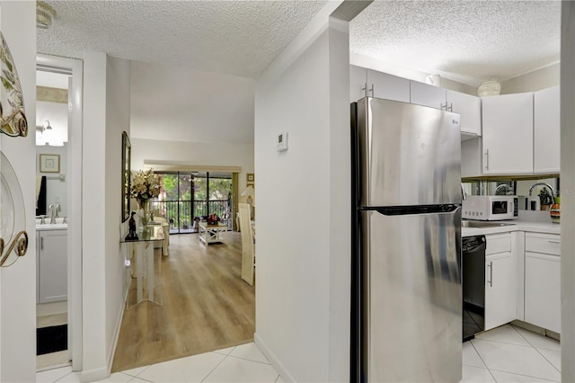 kitchen with stainless steel fridge, sink, light tile patterned floors, dishwasher, and white cabinetry