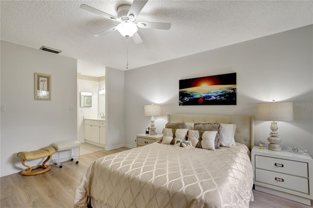 bedroom with a textured ceiling, ensuite bath, light hardwood / wood-style flooring, and ceiling fan