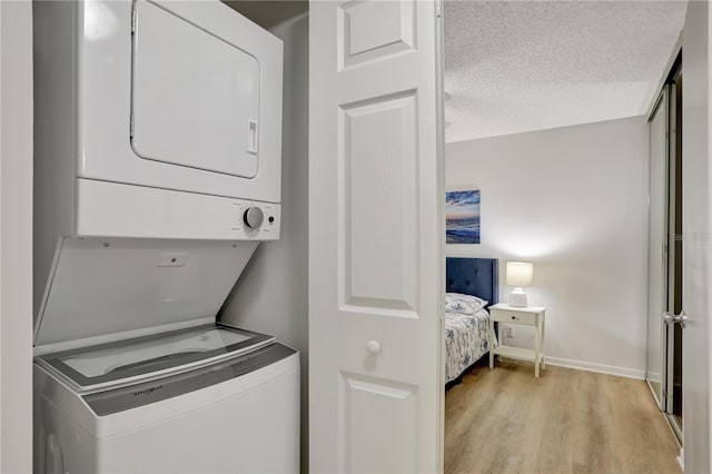 laundry area featuring a textured ceiling, light hardwood / wood-style floors, and stacked washer and clothes dryer