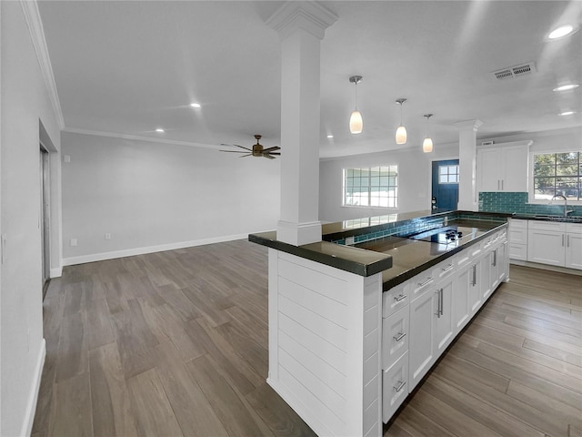 kitchen featuring white cabinets, black electric stovetop, decorative columns, and hanging light fixtures