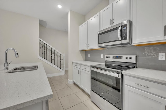 kitchen with light stone countertops, white cabinetry, sink, stainless steel appliances, and light tile patterned floors