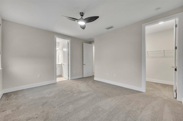 unfurnished bedroom featuring light colored carpet, ceiling fan, a spacious closet, connected bathroom, and a closet