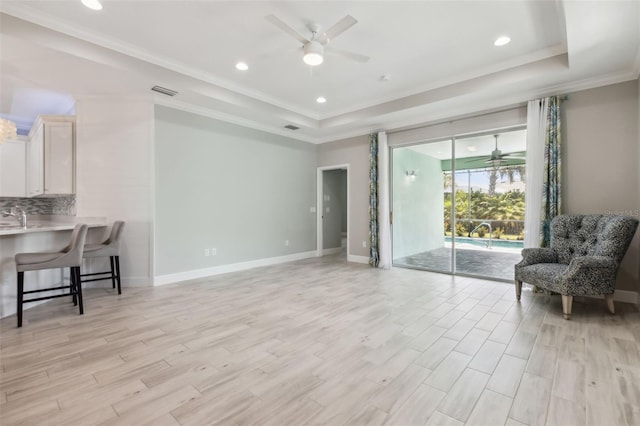 living room with a tray ceiling, ceiling fan, sink, and crown molding