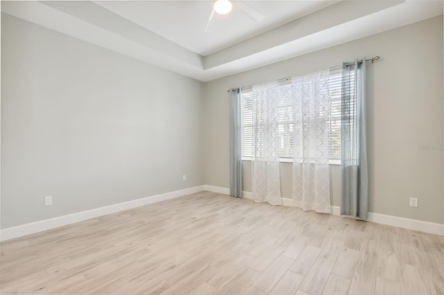 empty room with ceiling fan, a raised ceiling, and light hardwood / wood-style flooring