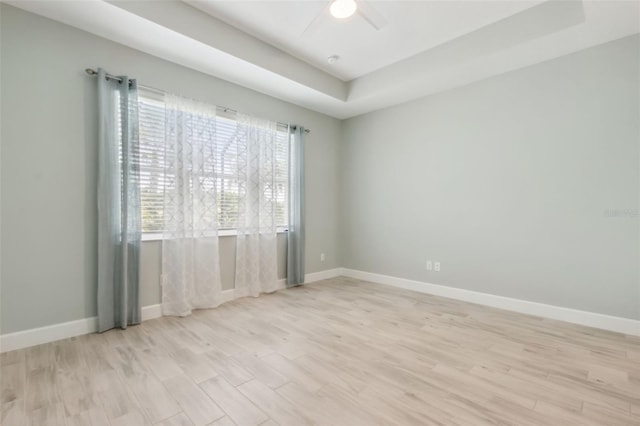 unfurnished room with a raised ceiling, ceiling fan, and light hardwood / wood-style flooring