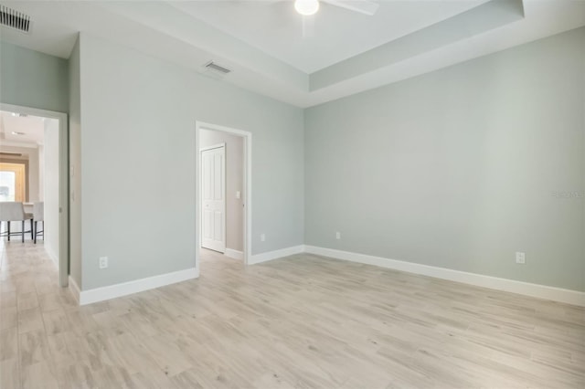 empty room featuring ceiling fan, a raised ceiling, and light wood-type flooring