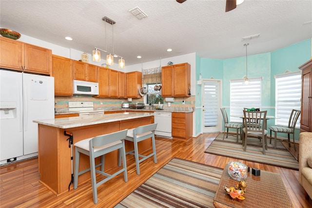 kitchen featuring a textured ceiling, a center island, white appliances, and hanging light fixtures