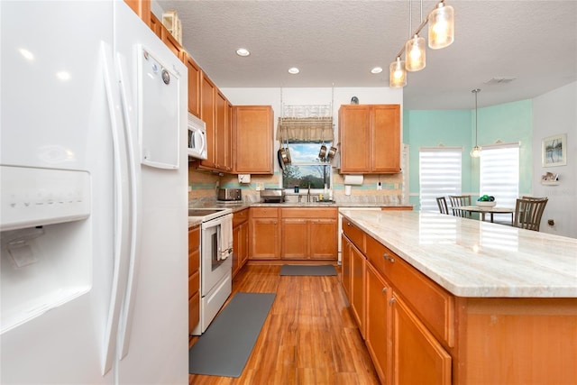 kitchen with a textured ceiling, white appliances, hanging light fixtures, and a healthy amount of sunlight