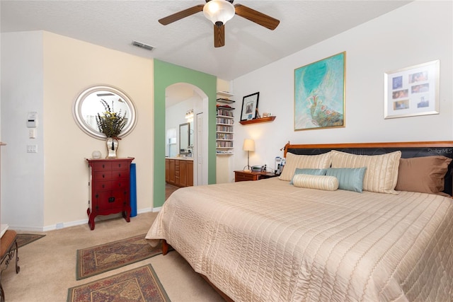 bedroom featuring a textured ceiling, light colored carpet, ensuite bath, and ceiling fan