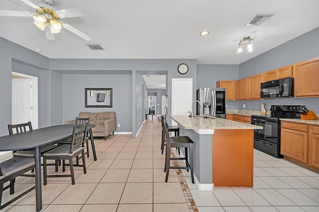 kitchen featuring a kitchen island with sink, black appliances, a kitchen breakfast bar, light tile patterned floors, and light stone counters