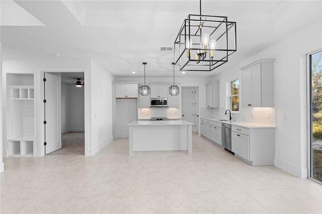 kitchen featuring ceiling fan with notable chandelier, stainless steel appliances, sink, a kitchen island, and hanging light fixtures