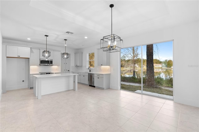 kitchen with white cabinetry, a kitchen island, decorative light fixtures, a water view, and appliances with stainless steel finishes