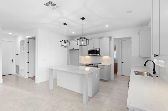 kitchen featuring appliances with stainless steel finishes, backsplash, sink, decorative light fixtures, and a center island