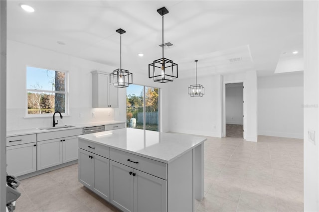 kitchen with gray cabinetry, a wealth of natural light, sink, a center island, and hanging light fixtures