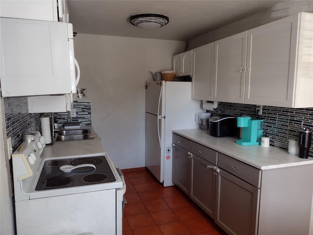 kitchen with white appliances, tile patterned floors, sink, decorative backsplash, and white cabinetry