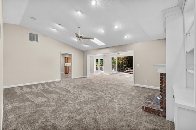 unfurnished living room with vaulted ceiling with skylight, a textured ceiling, ceiling fan, a fireplace, and carpet floors