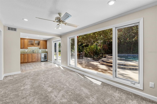 unfurnished living room with ceiling fan, french doors, beverage cooler, crown molding, and light carpet