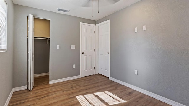 unfurnished bedroom with hardwood / wood-style flooring, a walk in closet, ceiling fan, and a closet