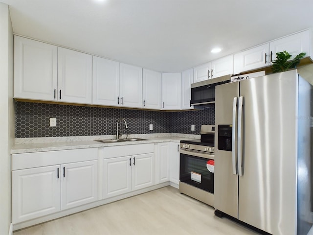 kitchen with white cabinets, sink, decorative backsplash, light hardwood / wood-style floors, and stainless steel appliances