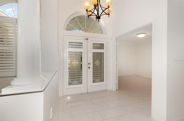 entryway with decorative columns, french doors, a towering ceiling, and a chandelier