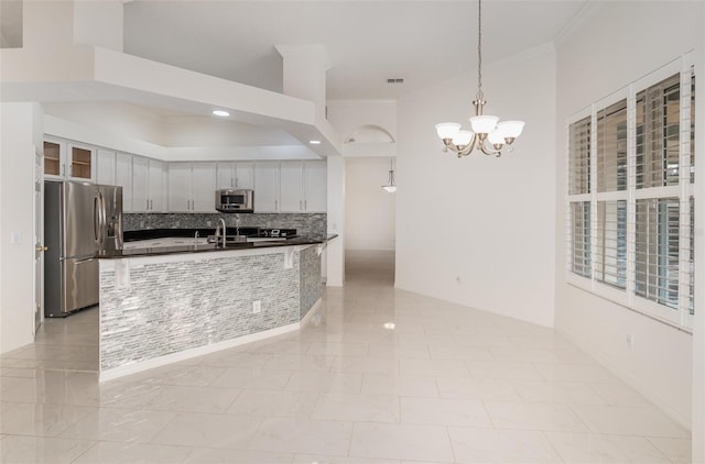 kitchen with hanging light fixtures, stainless steel appliances, a notable chandelier, kitchen peninsula, and ornamental molding