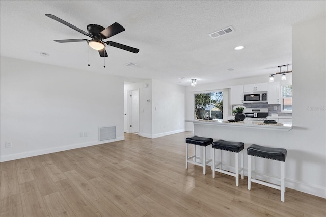 kitchen featuring a breakfast bar, white cabinets, kitchen peninsula, ceiling fan, and range