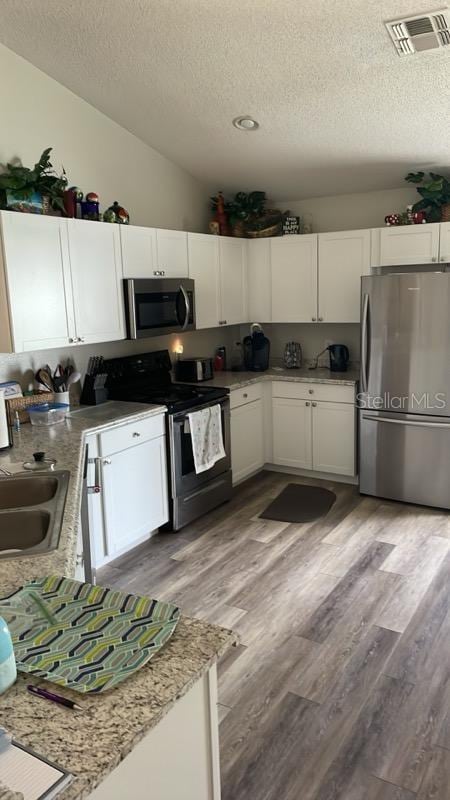 kitchen with a textured ceiling, light hardwood / wood-style floors, white cabinetry, and stainless steel appliances