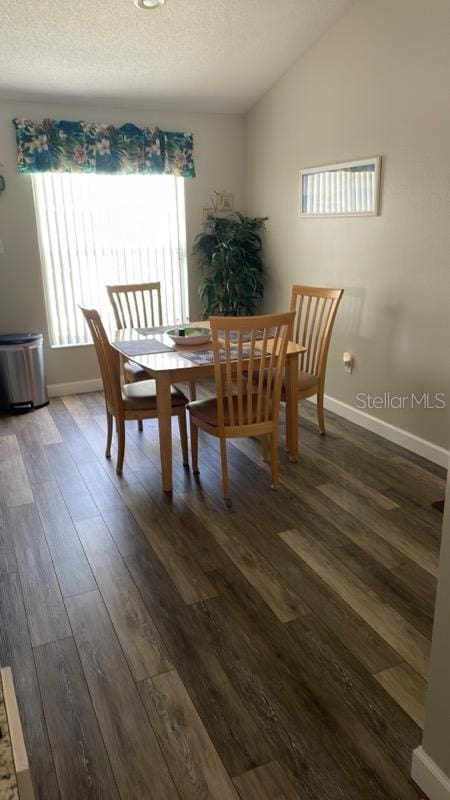 dining space with dark hardwood / wood-style flooring, a textured ceiling, and vaulted ceiling