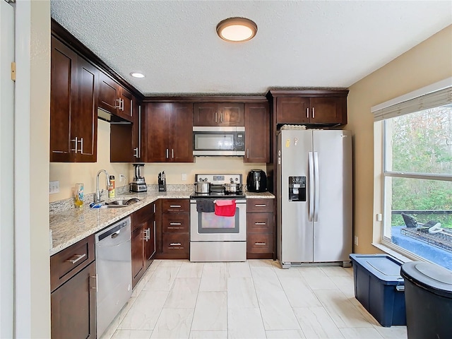 kitchen featuring a textured ceiling, stainless steel appliances, sink, light stone counters, and dark brown cabinets