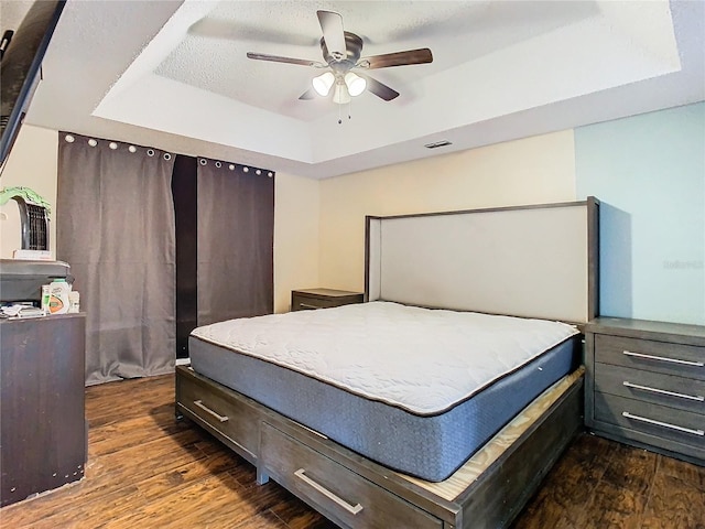 bedroom featuring ceiling fan, dark wood-type flooring, a textured ceiling, and a raised ceiling