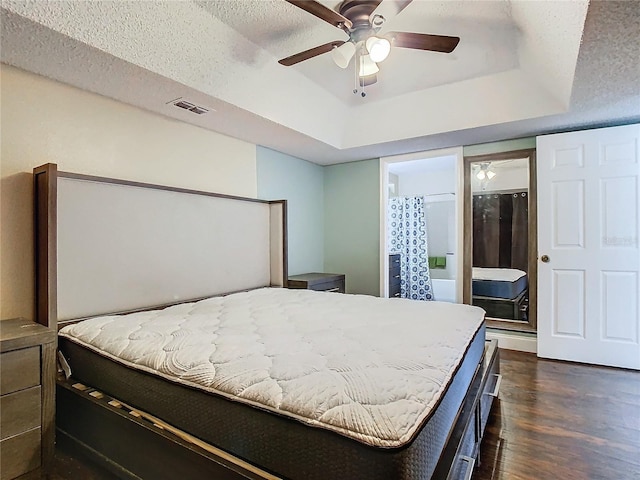 bedroom with ceiling fan, dark hardwood / wood-style flooring, a tray ceiling, and a textured ceiling