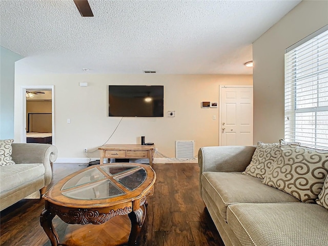 living room featuring ceiling fan, dark wood-type flooring, and a textured ceiling