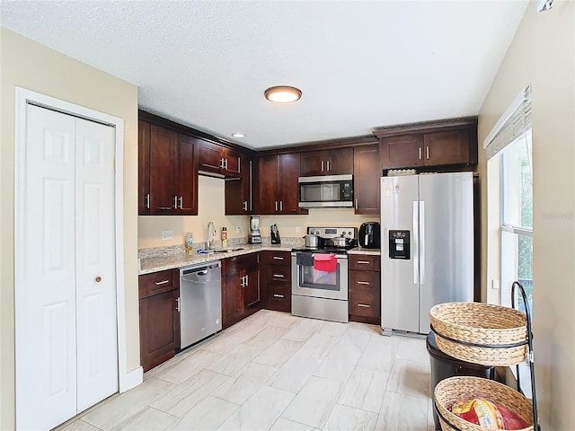 kitchen featuring stainless steel appliances, light stone countertops, a textured ceiling, dark brown cabinetry, and sink