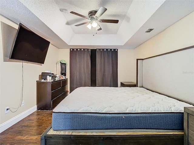 bedroom with ceiling fan, dark wood-type flooring, a textured ceiling, and a tray ceiling