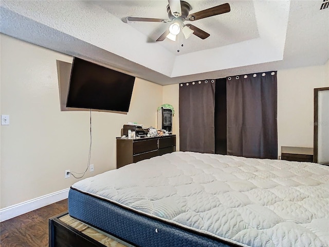 bedroom with a raised ceiling, ceiling fan, dark hardwood / wood-style floors, and a textured ceiling