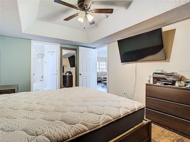 bedroom featuring ceiling fan, connected bathroom, wood-type flooring, and a tray ceiling